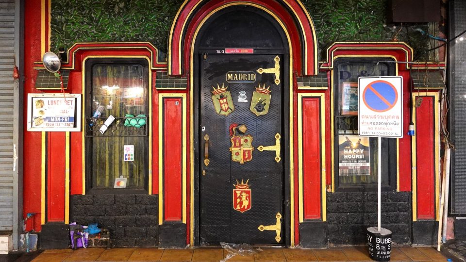Red and yellow arched façade with a black door bearing coats of arms and the word MADRID, green wall above.