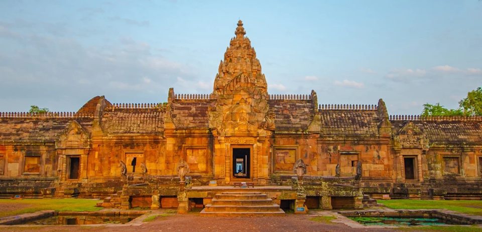 Khmer sanctuary in pink sandstone with an ornate central tower, stone-roofed galleries and an entrance stairway between two ponds.