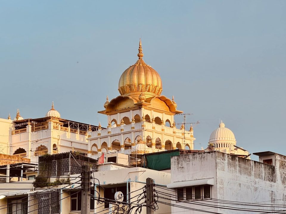 Gilded onion-shaped dome crowning a white arcaded building, rising above rooftops and tangled electric cables.