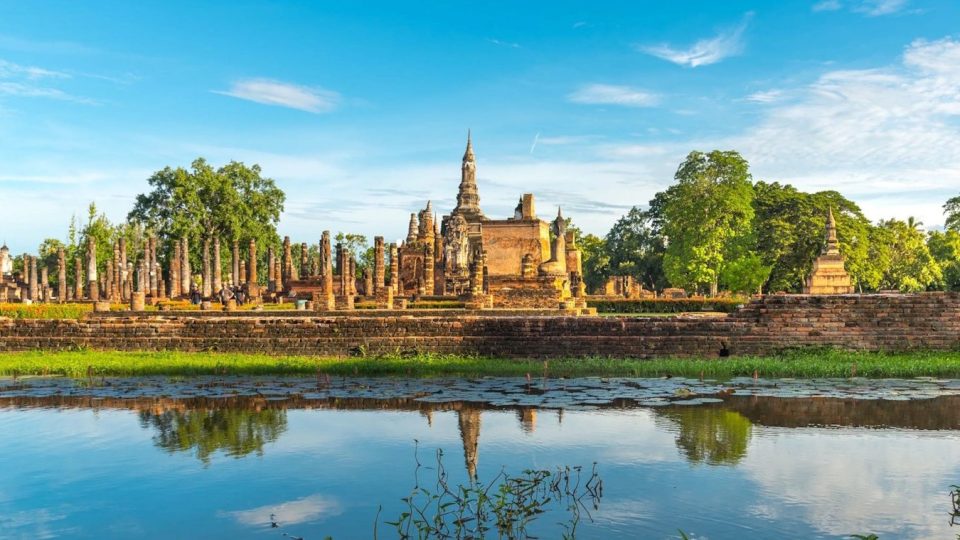 Brick temple ruins with a lotus-bud chedi, rows of columns and a pond reflecting the blue sky.